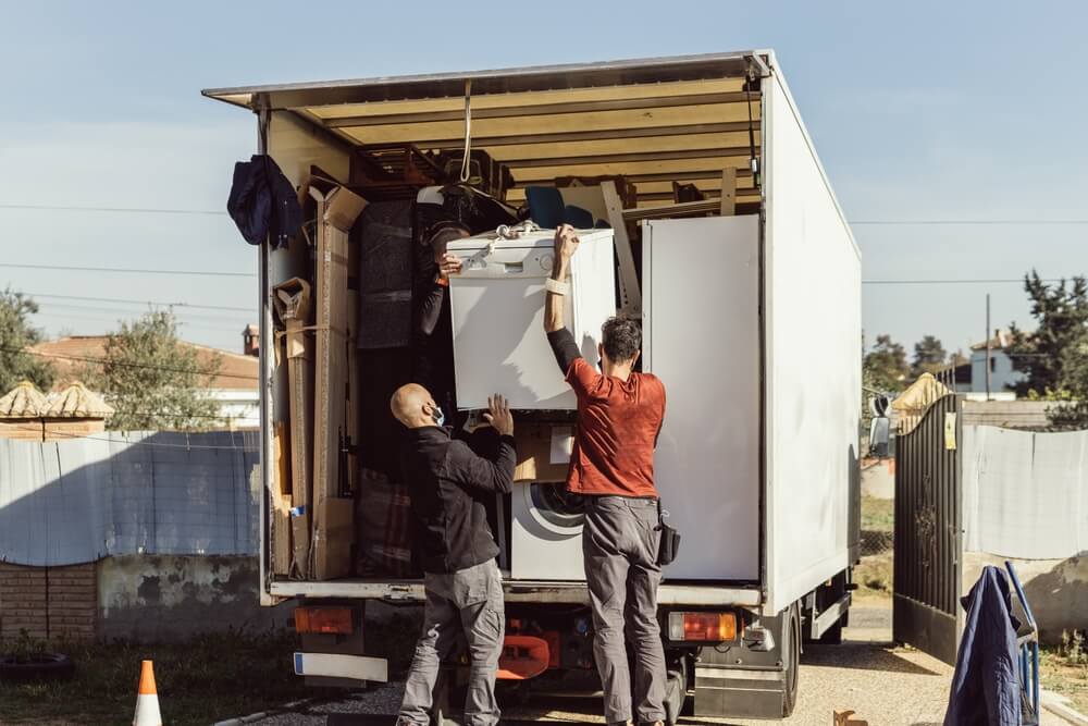 two movers lifting a fridge into the bed of a moving truck