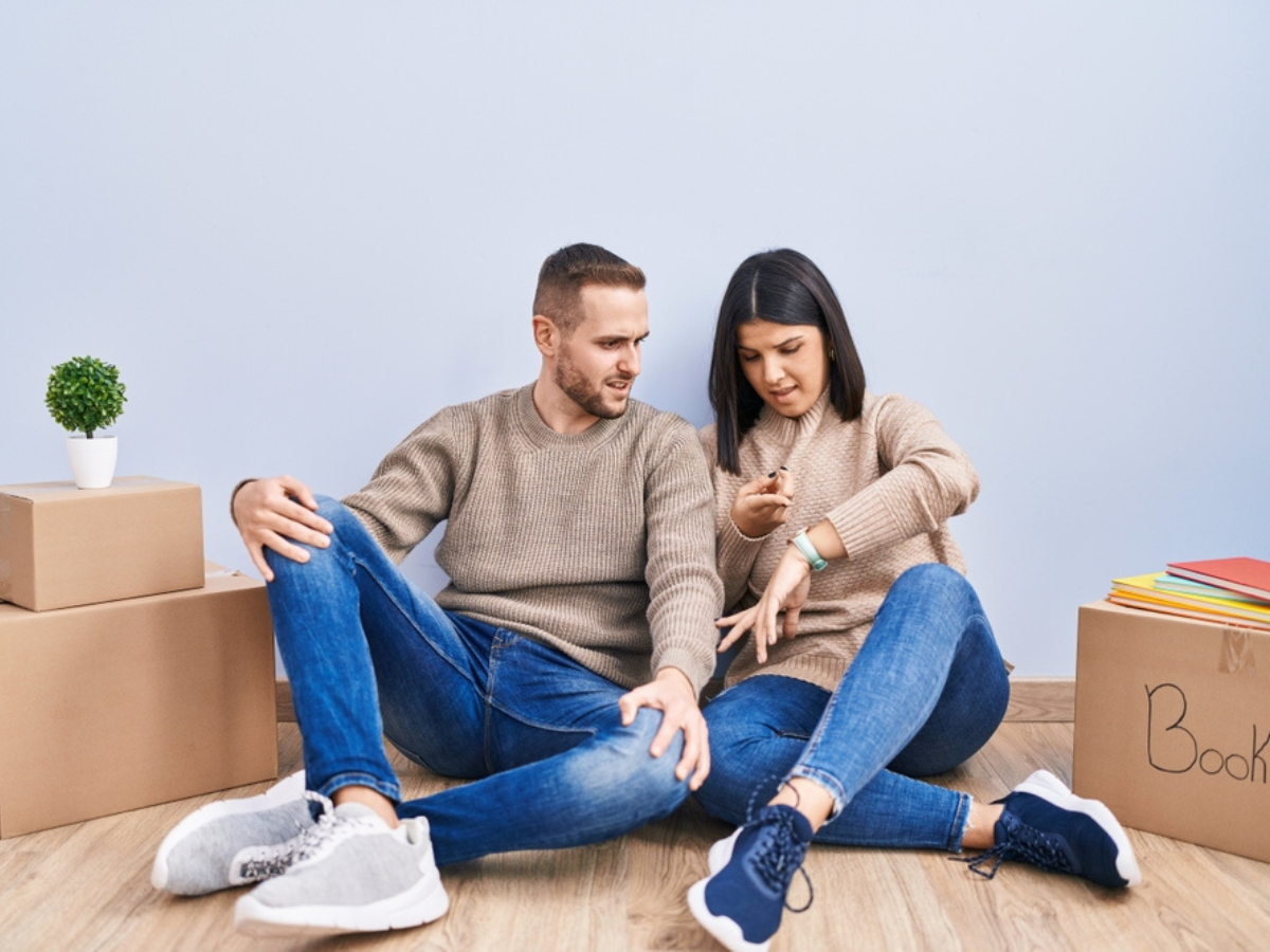 young couple sitting with moving boxes planning last-minute moving changes